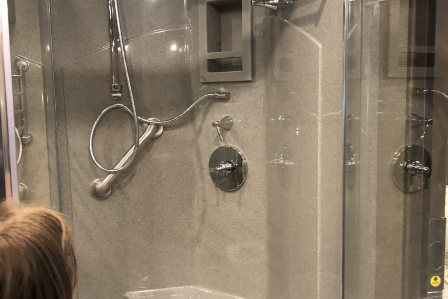 Modern RV rental shower with rainfall and handheld heads, integrated seat, and storage niche, ensuring comfort on the road.