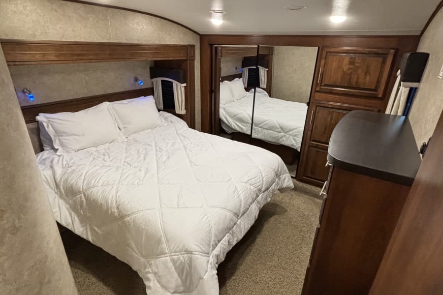 Cozy RV rental bedroom featuring a white bed, wood paneling, mirrored closet, and plush carpeting.