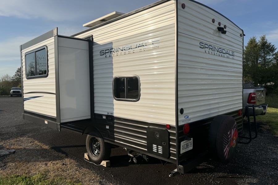 Experience a Springdale Keystone RV Mini travel trailer, ideal for an rv rental, shown parked outdoors with its slide-out extended.