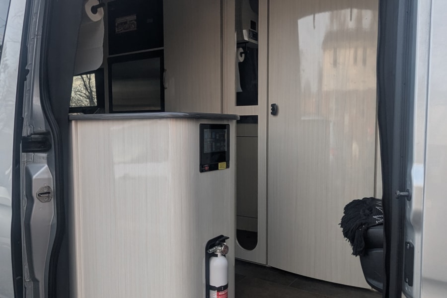 Interior of an rv rental camper van, showing a functional kitchen with cabinets, microwave, and a fire extinguisher.