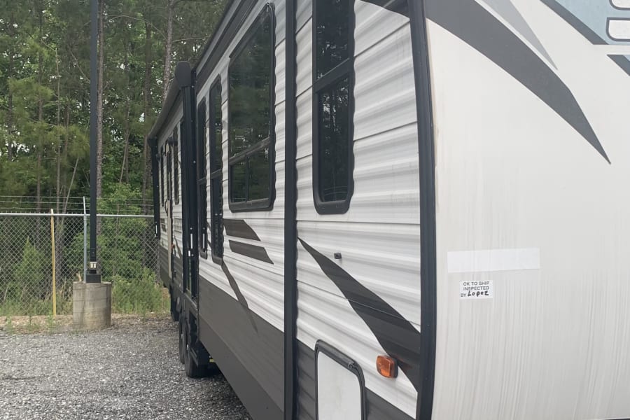 Side view of a white and black travel trailer RV rental, parked on gravel near trees, ready for a travel adventure.