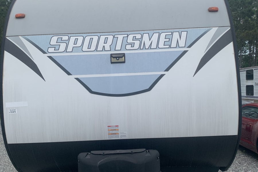 Front of a Sportsmen travel trailer, ideal for an rv rental. Shows gray and white exterior, hitch, and propane tanks.