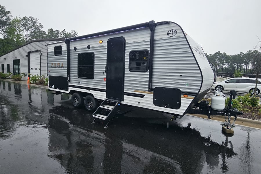 A grey Puma Camping Edition travel trailer, ideal for rv rental, sits on a wet lot with its steps down on a rainy day.