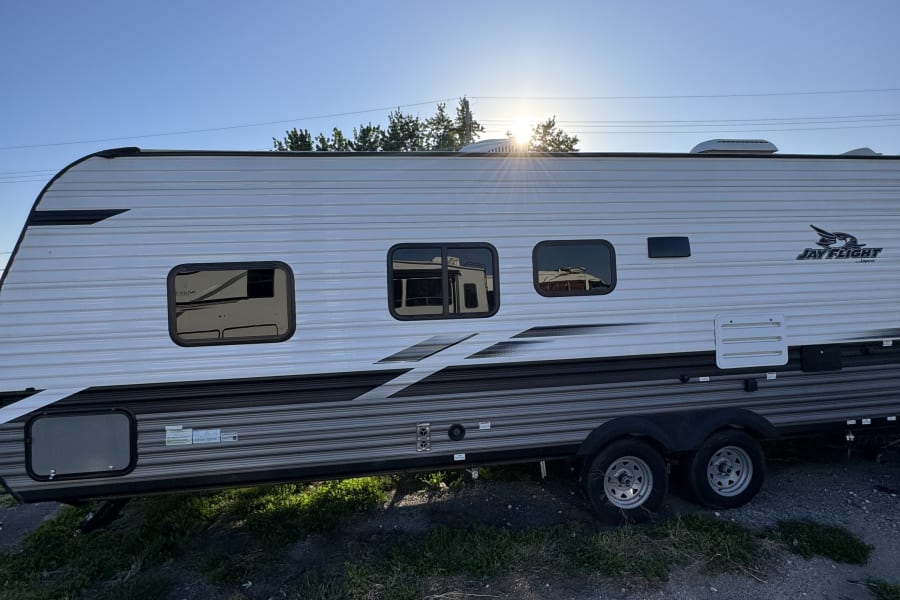 Experience outdoor freedom with this bright Jayco travel trailer RV rental, parked on gravel under a sunny blue sky.
