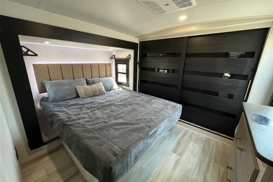Spacious, modern RV rental bedroom featuring a large bed, elegant dark closet, and contemporary decor for comfortable travel.