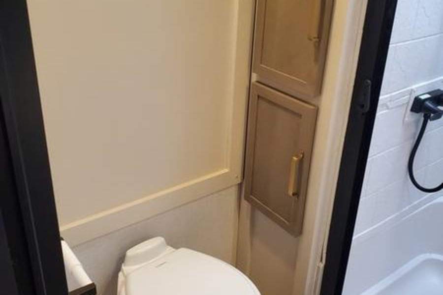 Inside an RV rental bathroom: white toilet, light wood cabinets, and shower stall. Efficient, compact design.