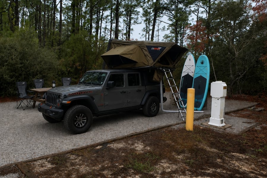 Adventure-ready RV rental: Jeep Gladiator with rooftop tent, paddleboards, and campsite setup for overlanding fun!