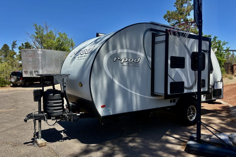 This light gray R-Pod travel trailer is a compact rv rental option, perfect for camping trips. It's parked outdoors on a sunny day.