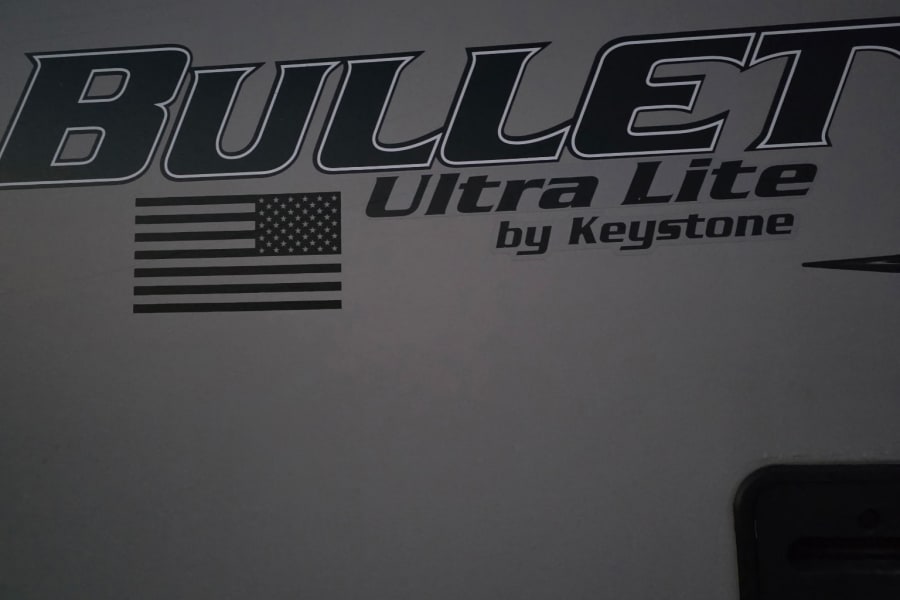 Close-up of a Bullet Ultra Lite by Keystone RV's side, showing its branding and an American flag, often seen in rv rental fleets.