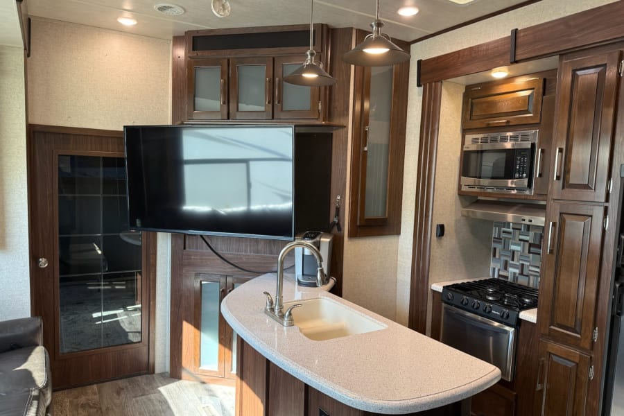 Modern rv rental with full kitchen: stove, microwave, island sink, and living area with TV.