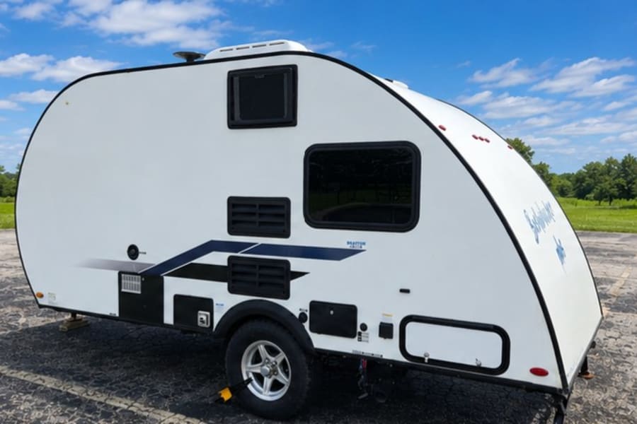 Explore in this stylish white teardrop **RV rental**, a compact camper with black trim & blue graphics, parked outdoors.