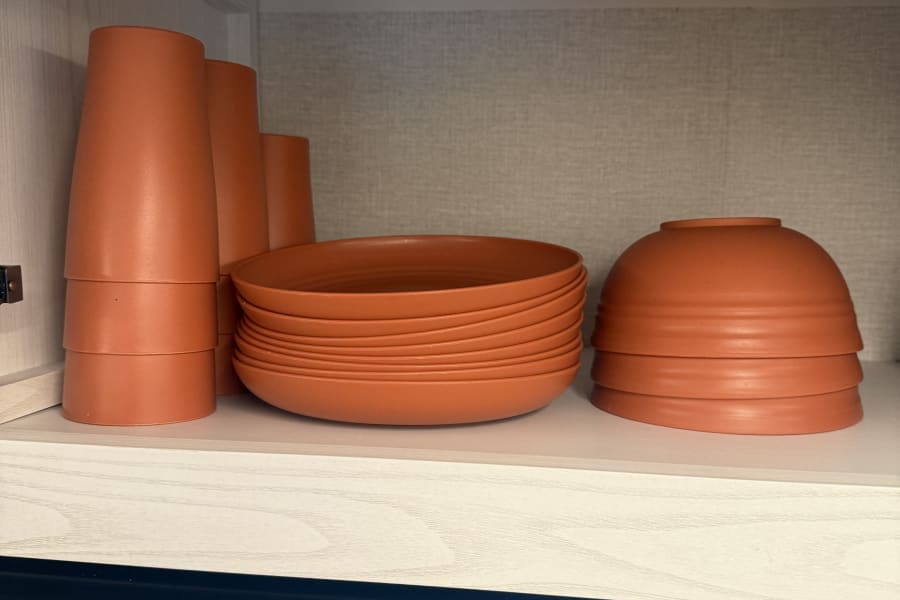 RV rental kitchen: Stacked orange cups, plates, and bowls neatly stored in a light wood cabinet above a range.