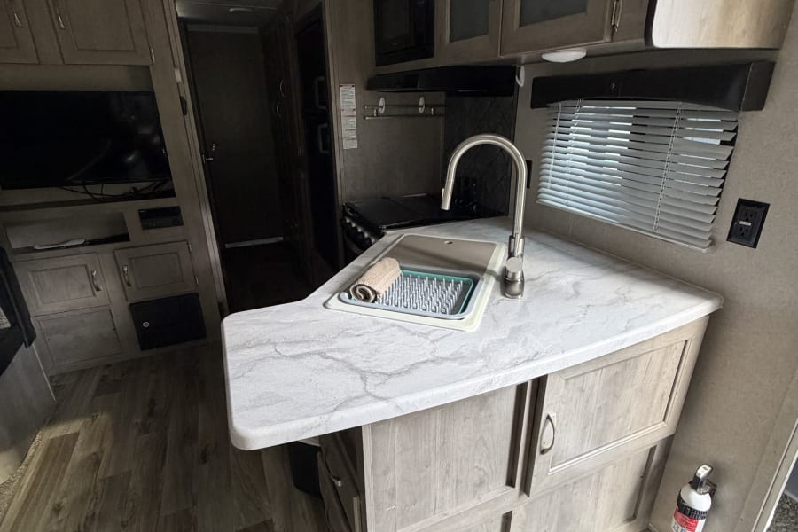 RV rental interior: well-equipped kitchen with sink, microwave, stove, modern cabinets, TV, and wood-look flooring.