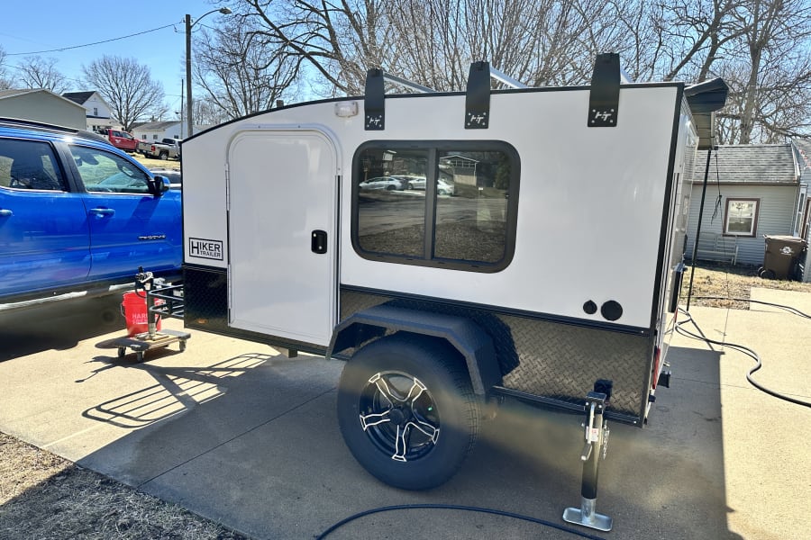 A white Hiker Trailer RV rental is parked with a blue pickup truck on a sunny driveway, ready for adventure.