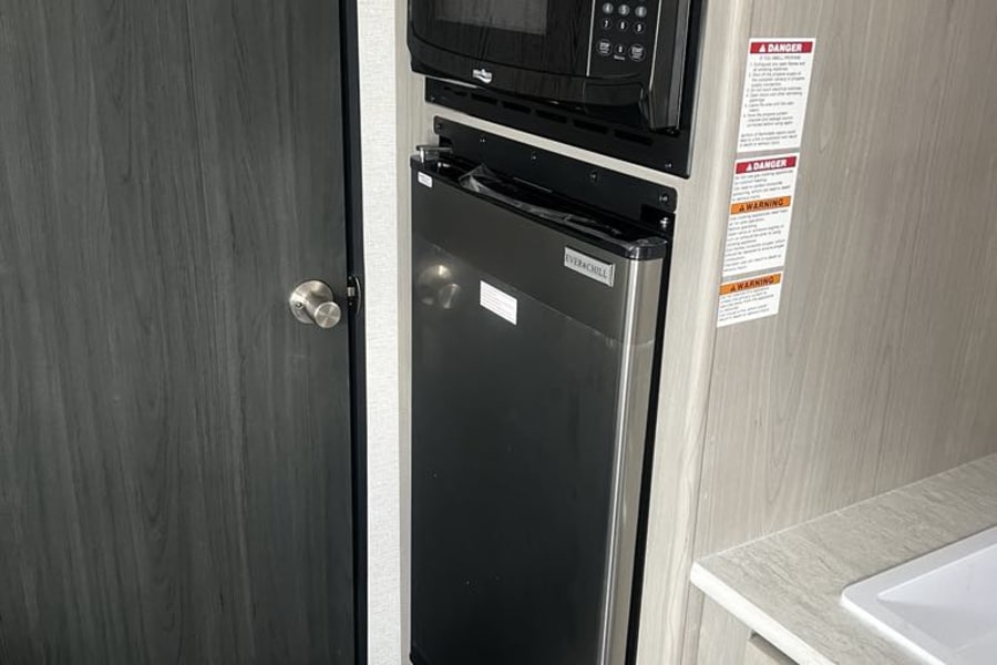RV rental kitchen: A built-in black microwave is mounted above a slim, stainless steel Everchill refrigerator, optimizing space.