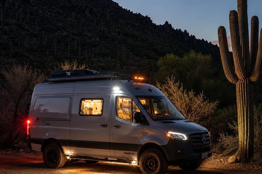 An illuminated Winnebago Revel camper van sits in a desert scene at night, ready for your next RV rental adventure.
