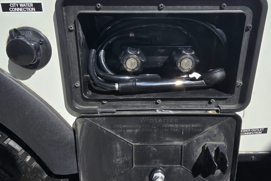 This RV rental exterior shows the city water connection, outdoor shower station, and winterizing instructions.
