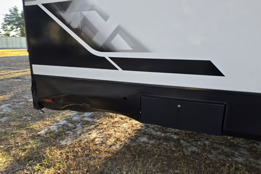 RV rental: Lower side of a trailer showing damage on the rear black skirt/fender and an exterior storage compartment.