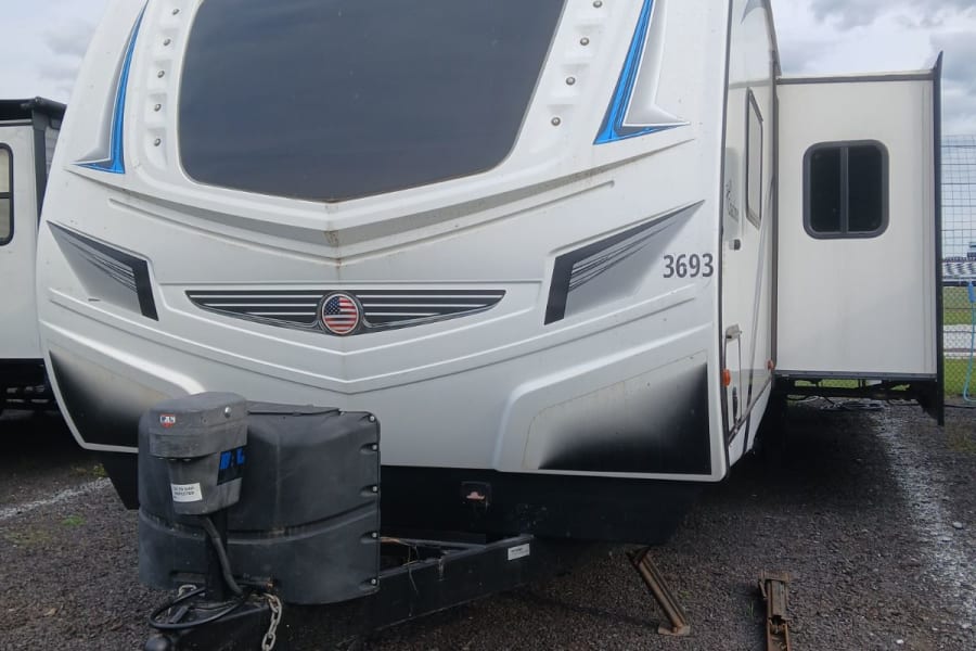 White Coachmen Freedom Express travel trailer RV rental with slide-out extended, parked on gravel under a cloudy sky.