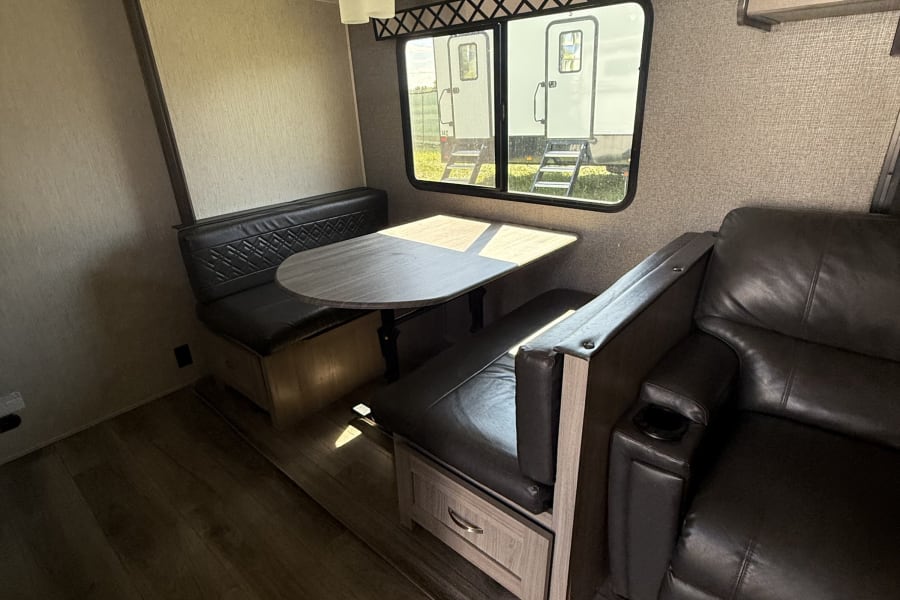 Spacious RV rental interior with dinette, comfy recliners, and wood-look flooring. Perfect for your next adventure!