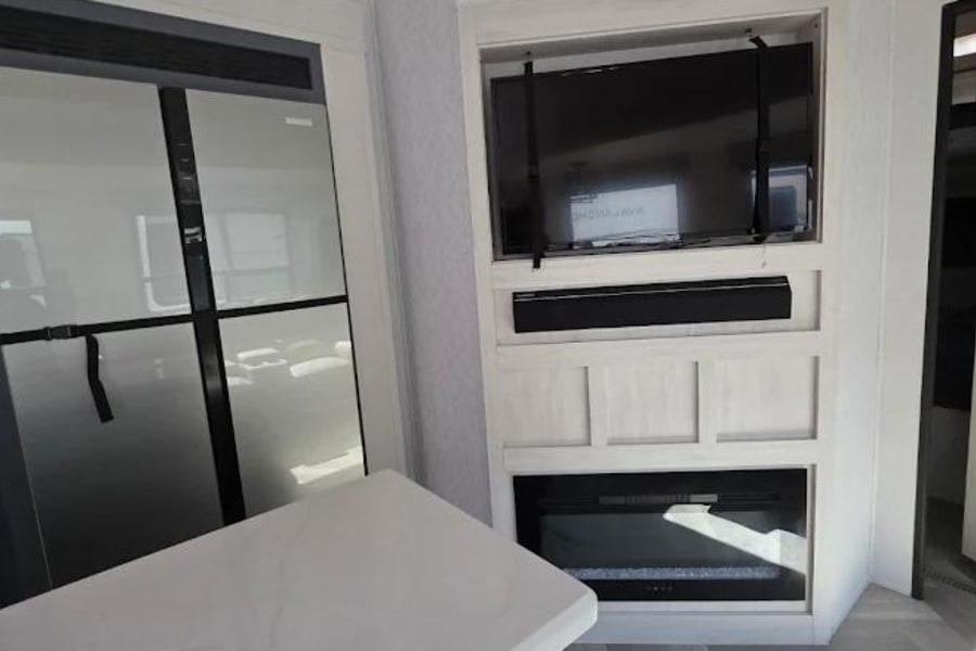 This modern RV rental features a living area with a TV, electric fireplace, spacious kitchen counter, and fridge.