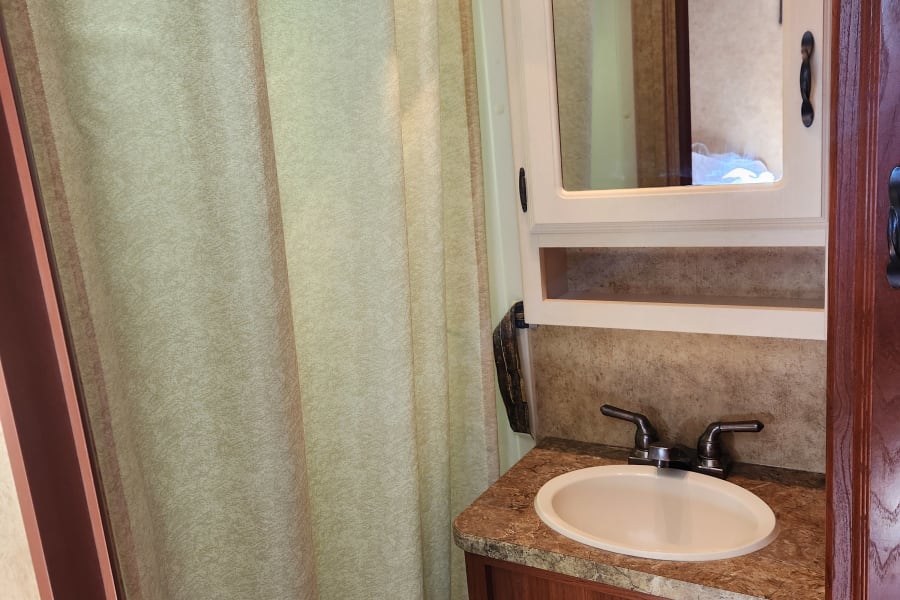 This RV rental bathroom features a compact vanity with sink, mirror cabinet, and shower with a patterned curtain.