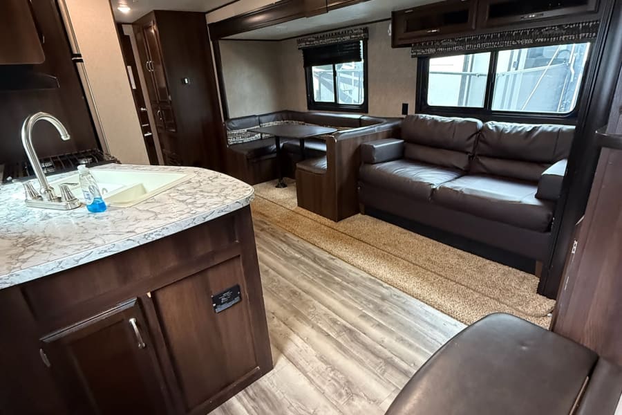 Modern RV rental interior with kitchen, living room sofa, and dinette seating. Ready for your next travel adventure!