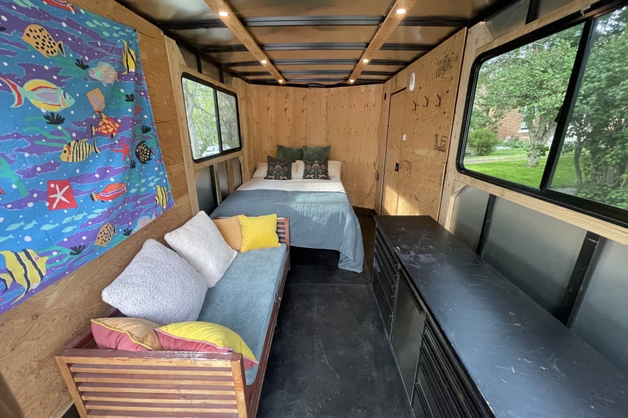 Cozy rv rental camper interior featuring a bed, vibrant couch, wood paneling, and outdoor views through windows.
