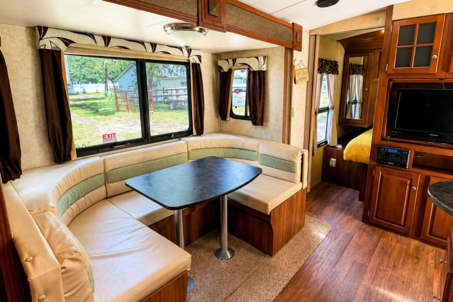 RV rental: Bright interior with curved dinette, wood floor, entertainment center, and windows with outdoor views.