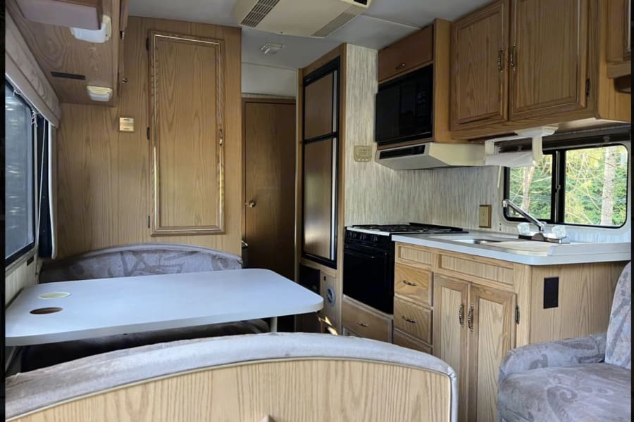 Cozy rv rental interior: dining booth, full kitchen with microwave, stove, sink, & wood cabinets. Ready for your adventure.