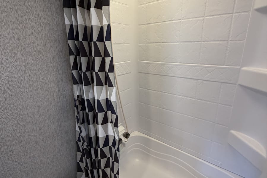 RV rental bathroom showing a white toilet, shower/tub combo, and a stylish black and white geometric shower curtain.