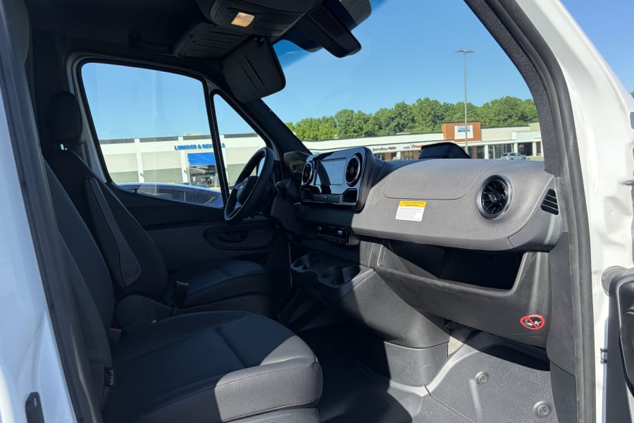 Interior view of a modern van or RV rental cab, featuring the dashboard, steering wheel, and front seats on a sunny day.