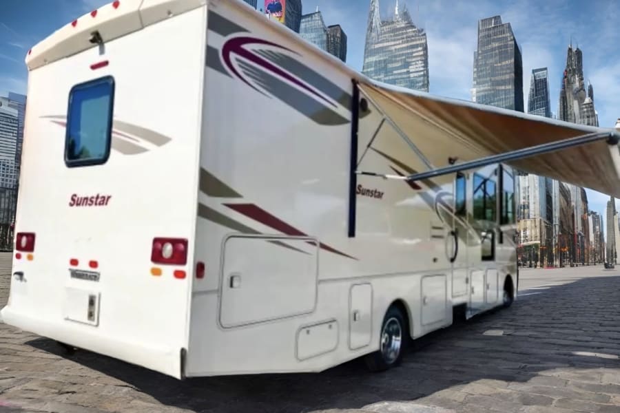 A white Sunstar rv rental with extended awning in a city street with tall buildings in the background, ready for travel.