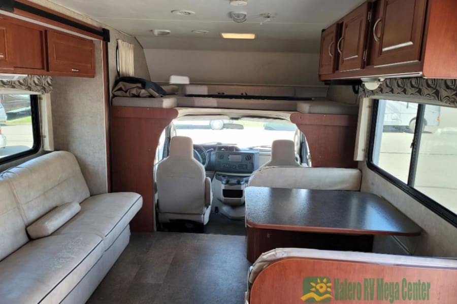 View inside an RV rental showing dinette, sofa, overhead cabinets, and front bunk bed. Spacious Class C motorhome.