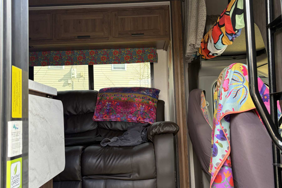 Inviting RV rental interior: brown recliner, colorful pillows, window view, and bunk ladder with bright blankets.