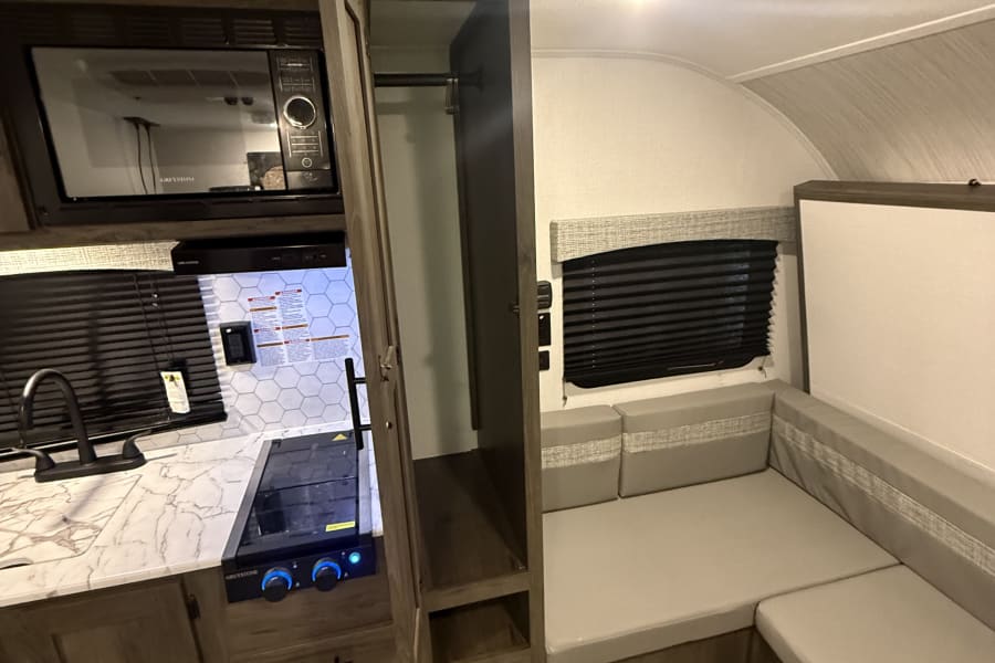 RV rental: compact kitchen with microwave, sink, stove, plus a built-in dinette seating area and closet.