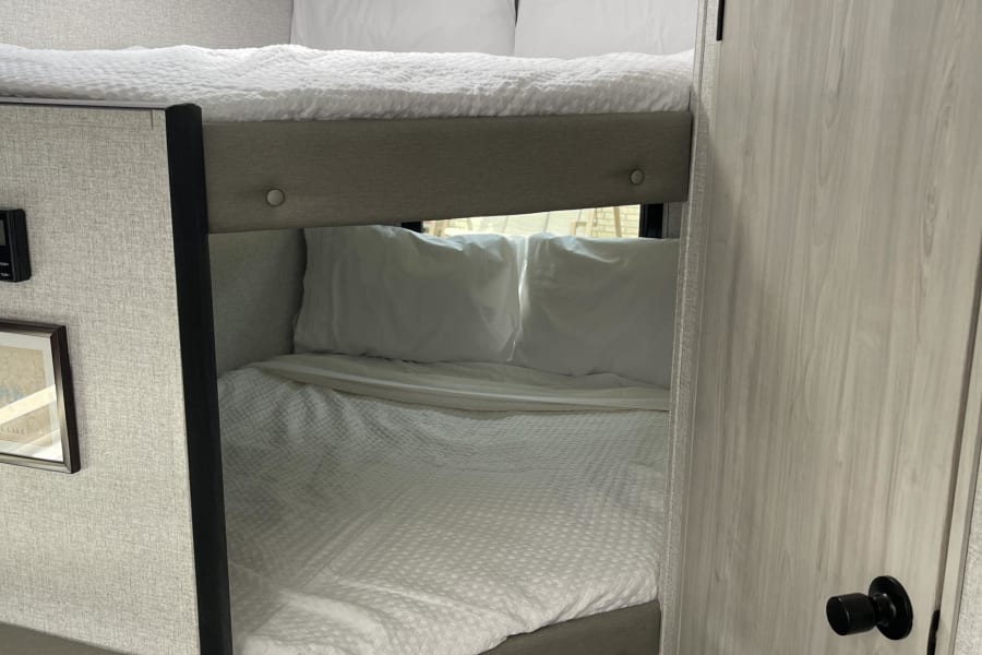 Cozy bunk beds with white bedding inside a modern RV rental, offering comfortable sleeping arrangements for travelers.