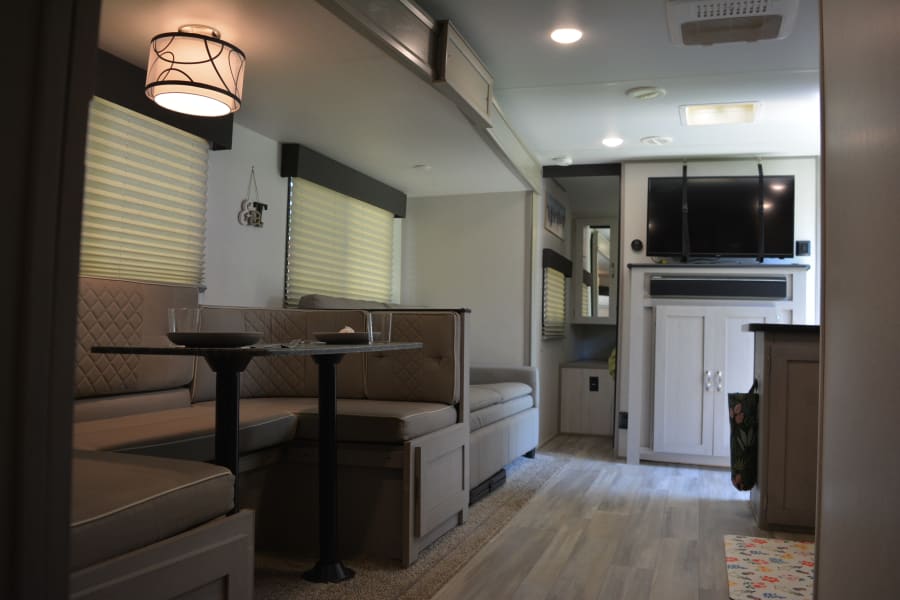 Bright RV rental interior featuring a cozy dinette, modern kitchen counter, and entertainment area with a TV.