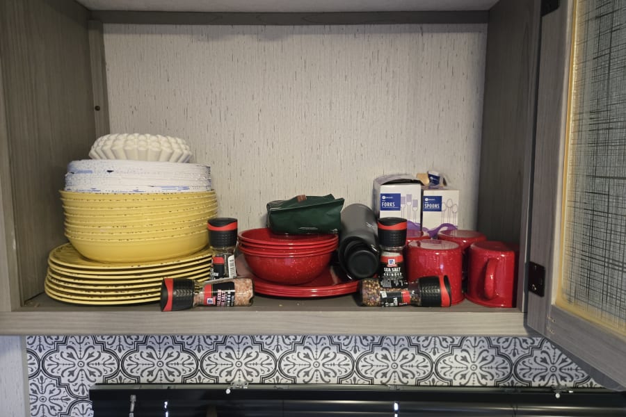 An rv rental kitchen cabinet filled with neatly stacked yellow & red dishes, mugs, and essential spices.