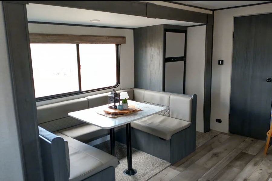 Inside a modern rv rental: U-shaped dinette, window, fridge, and stylish decor. Ready for your travels.