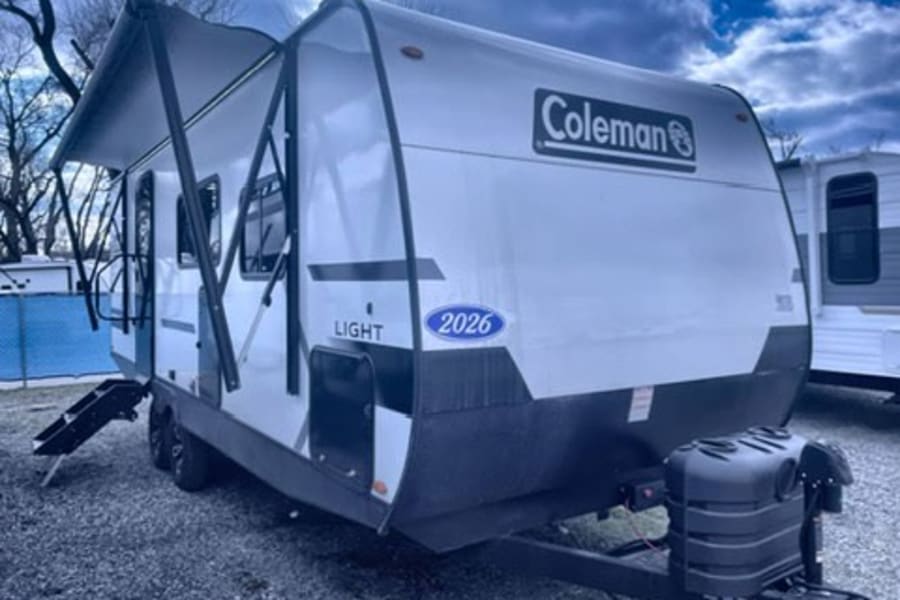 Explore with this Coleman travel trailer rv rental! White RV, awning extended, steps visible. Perfect for outdoor camping adventures.