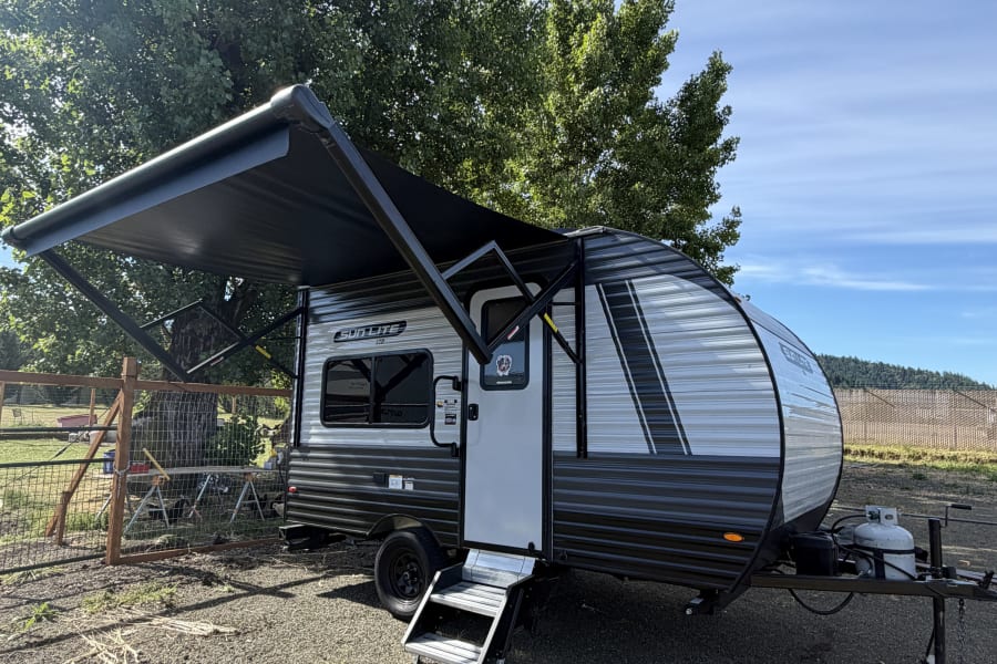 Experience nature with this modern rv rental. A sleek black and silver travel trailer with an extended awning, under clear skies.