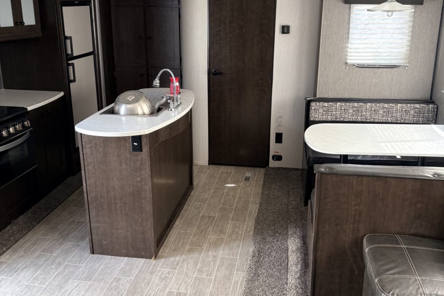 Modern RV rental interior with a kitchen island, dining booth, sofa, and wood-look flooring. Perfect for your next adventure.