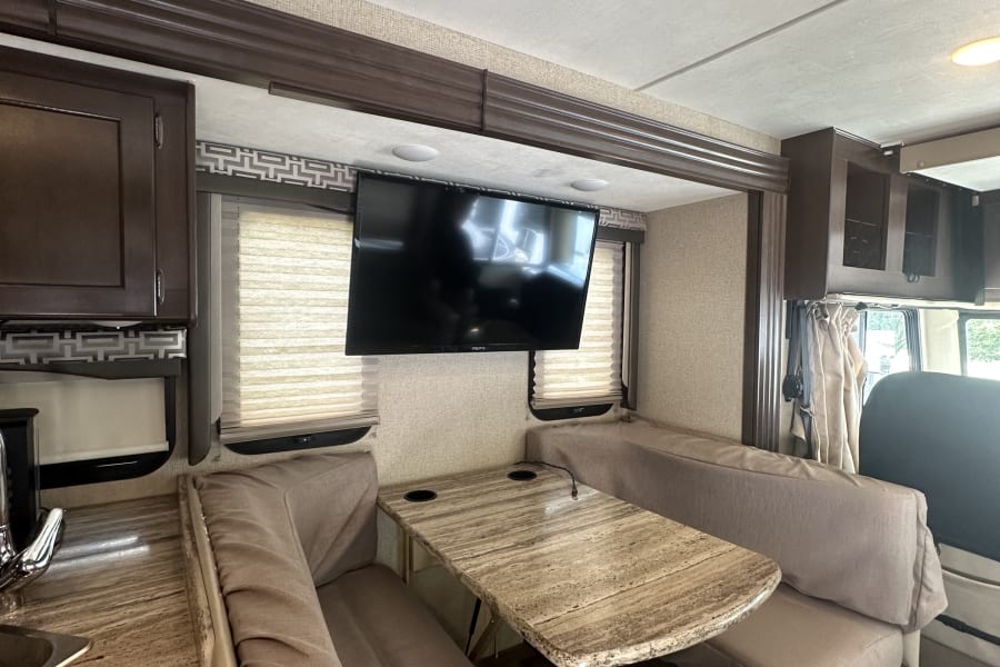 This inviting rv rental interior features a cozy dinette with a wall-mounted TV, kitchen counter, and comfortable benches.