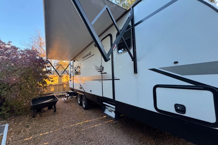 Side view of a white Minnie RV rental with its awning extended, parked on gravel.