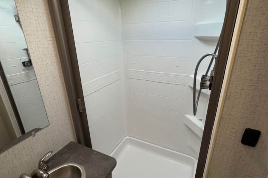 RV rental bathroom features a modern shower, skylight, compact sink, and mirror, designed for comfort on the road.