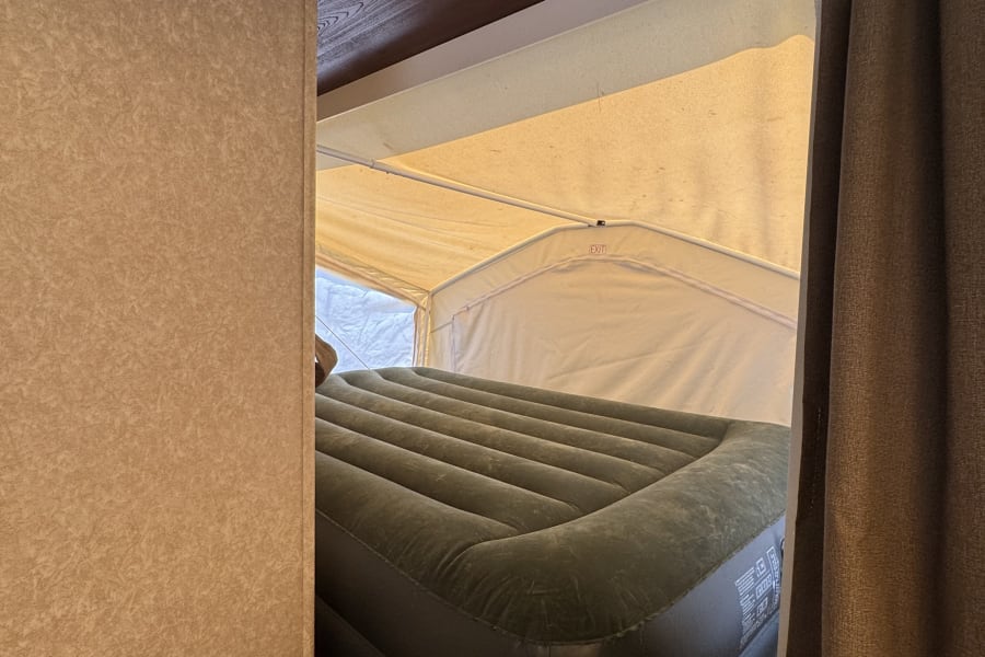 Inside an RV rental, an inflatable air mattress fills a pop-up camper bunk, with canvas walls and a brown curtain.