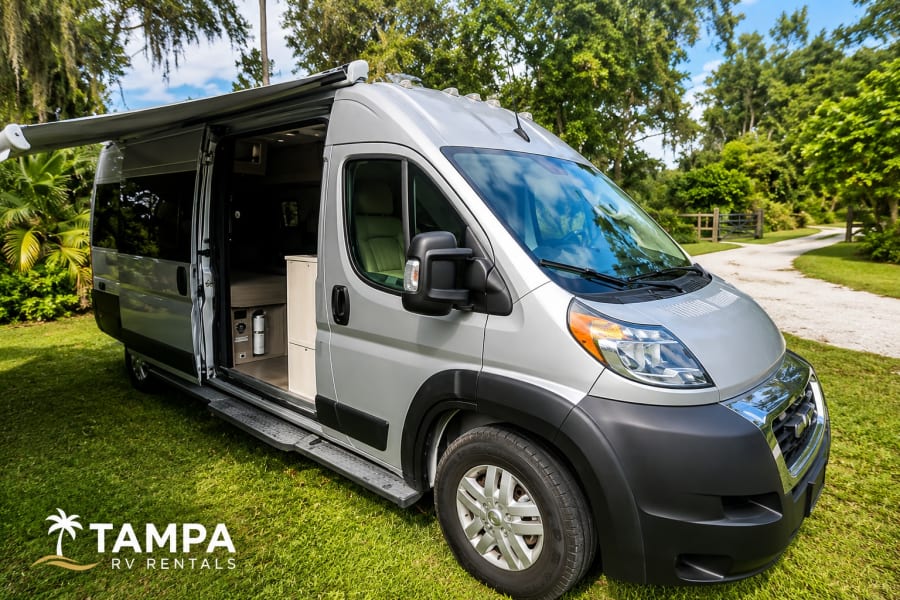 Silver camper van RV rental on grass with open door & extended awning, ready for outdoor adventure.