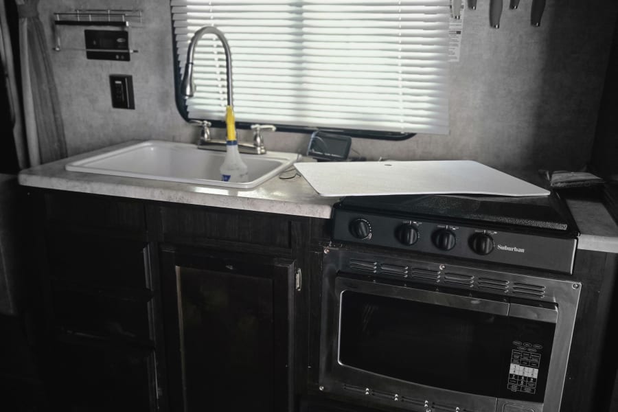 This RV rental kitchen features a sink, Suburban stove, microwave, and wall-mounted knives, ideal for travel cooking.