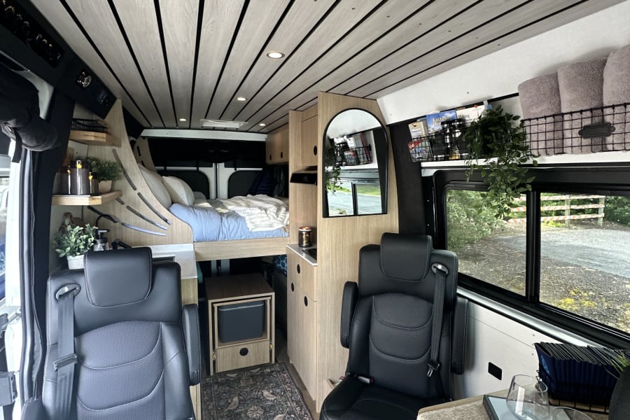 Step into this modern **rv rental**! The cozy campervan interior features a wood-slat ceiling, raised bed, kitchen unit, and swivel seats.